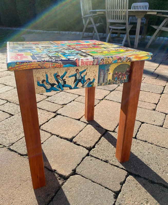 A wooden table with Beatles comic artwork across its top and sides, photographed outdoors.